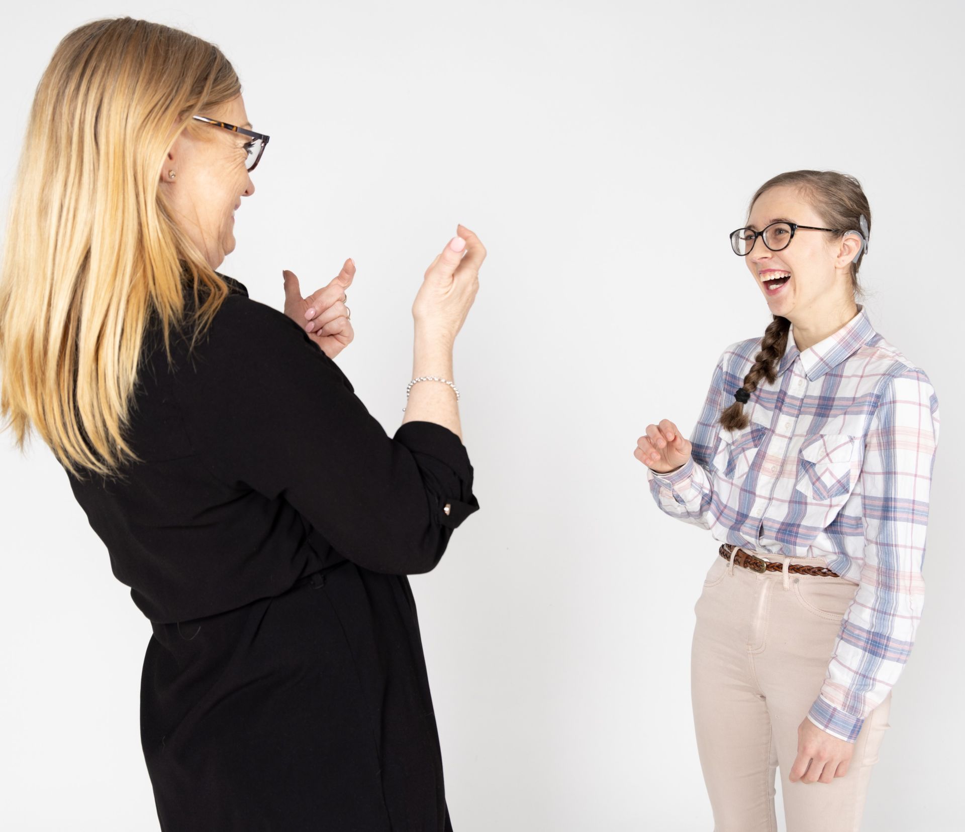 Two women smiling and communicating in sign language, one wearing a hearing device